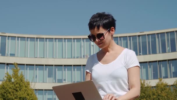 Young business woman sitting in front of an office building and working on a computer — Stock Video