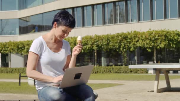 Obchodní žena s icecream sedí před úřední budovy a pracuje na počítači — Stock video