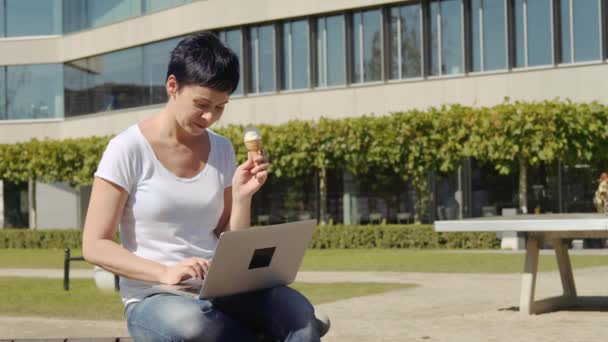 Business woman with icecream sits in front of an office building and works on a computer — Stock Video