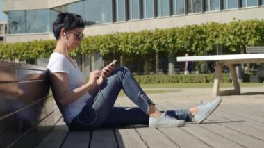 iş kadını bir beyaz T-shirt bir ofis binası önünde oturur ve müzik dinliyor