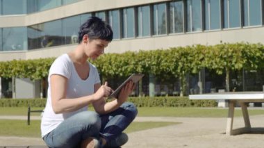 bina ve bir tablet üzerinde çalışan bir işyeri önünde oturan beyaz tişört kadında