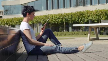 bina ve bir tablet üzerinde çalışan bir işyeri önünde oturan beyaz tişört kadında