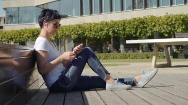 iş kadını bir beyaz T-shirt bir ofis binası önünde oturur ve müzik dinliyor