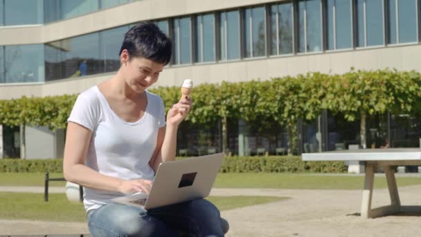 Obchodní žena s icecream sedí před úřední budovy a pracuje na počítači — Stock video