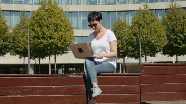 Donna d'affari seduta di fronte a un edificio per uffici e che lavora su un computer — Video Stock