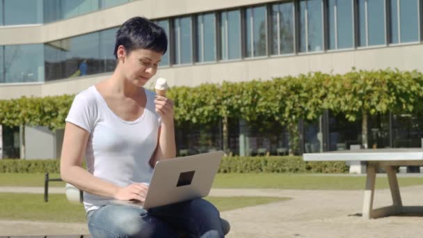 Obchodní žena s icecream sedí před úřední budovy a pracuje na počítači — Stock video