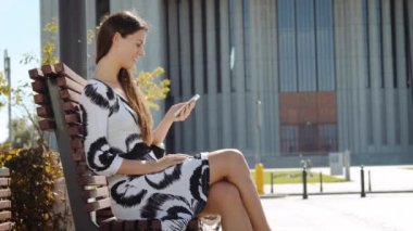 El ve çalışan bir telefon ile bir bankta oturmuş bir elbiseli Genç iş kadını