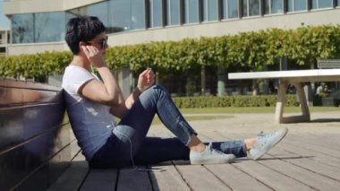 iş kadını bir ofis binası önünde oturur ve telefonda müzik dinler