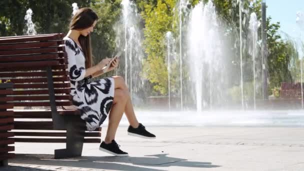 Giovane donna d'affari in un vestito seduta su una panchina e lavora su un tablet — Video Stock