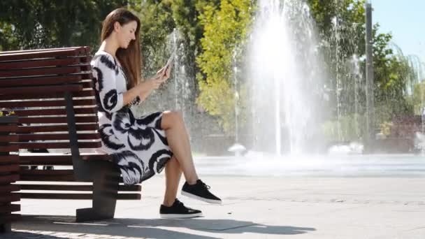 Young business woman in a dress sitting on a bench and talking on the tablet — Stock Video