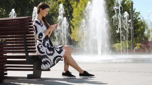 Ung affärskvinna i en klänning sitter på en bänk och prata i telefon — Stockvideo