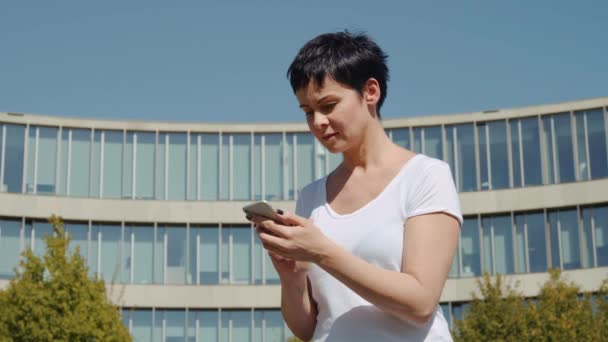 Mujer de negocios sentada frente a un edificio de oficinas y escribiendo un mensaje por teléfono — Vídeo de stock