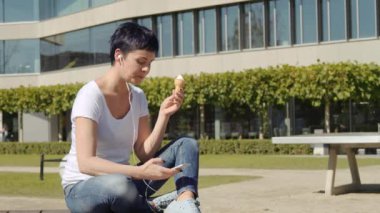 kadın dondurma ile bir ofis binası önünde oturur ve telefonda müzik dinler
