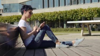 iş kadını bir ofis binası önünde oturur ve telefonda müzik dinler