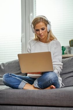güzel genç kadın ve bir bilgisayar ve müzik dinler bir kanepede oturan bir kadın