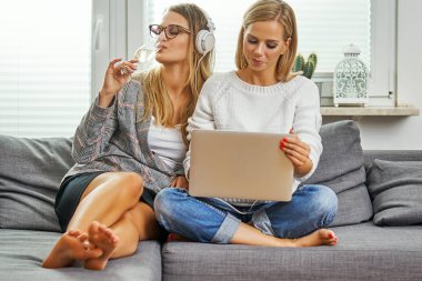 iki genç kadın ve kadın oturup bir kanepede bir bilgisayar ve müzik dinlemek