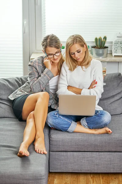 two young and women are sitting on a couch with a computer and reading a sad message