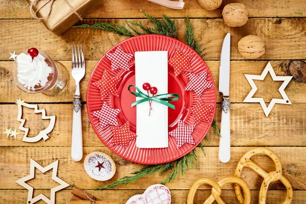 Фон кануна Рождества на старом деревянном столе с красной тарелкой с ножом и вилкой — стоковое фото