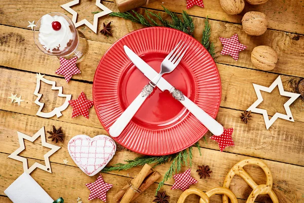 Christmas Eve background on an old wooden table with a red plate with a knife and fork — Stock Photo, Image