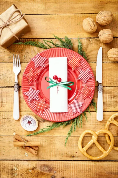 Фон кануна Рождества на старом деревянном столе с красной тарелкой с ножом и вилкой — стоковое фото
