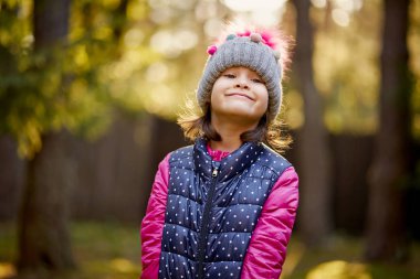 bir kap ve ceket, sevimli küçük kız bir parkta bir sonbahar orman çim üzerinde duruyor