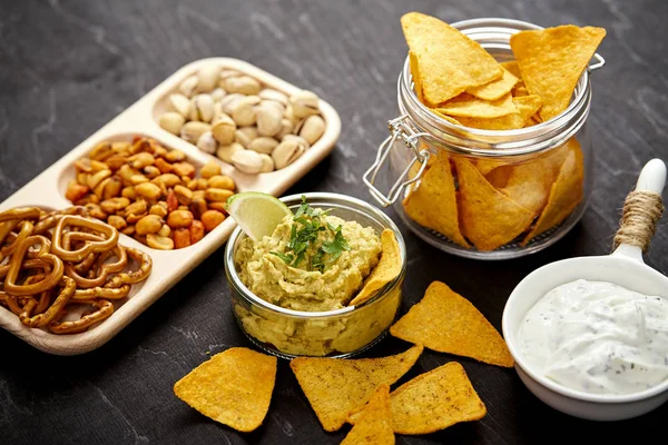 Ciotola di vaso di guacamole con nachos e snack salati su un vecchio tavolo di legno nero — Foto Stock