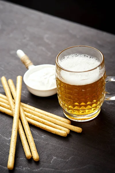 Birra dorata e deliziosi snack salati su un vecchio tavolo di legno nero — Foto Stock