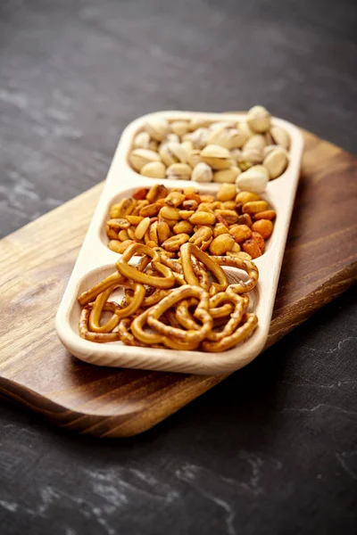 Plate with delicious pistachio pretzels and peanuts on an old black wooden table — Stock Photo, Image