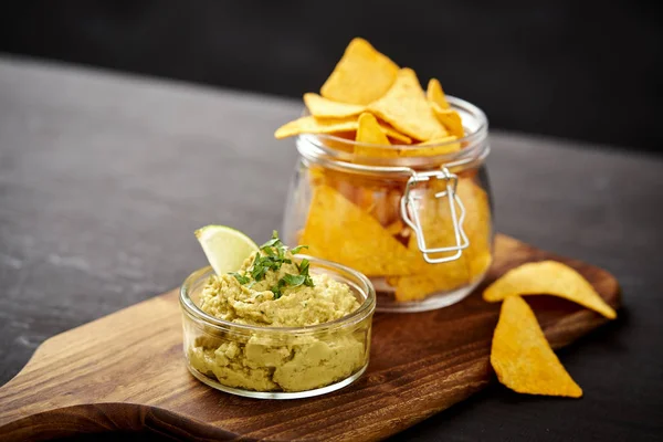 Ciotola di guacamole fresco delizioso e un barattolo di nachos su un vecchio tavolo di legno nero — Foto Stock