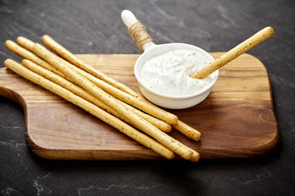 Delicious salty sticks and garlic dip on an old black wooden table — Stock Photo, Image