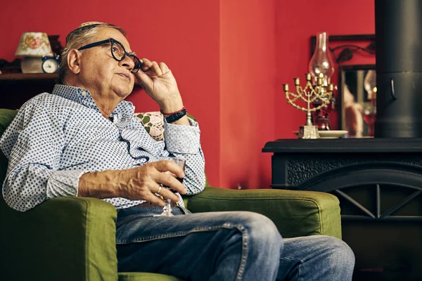 Страшный еврейский старший в кресле, пьющий кошерное вино — стоковое фото