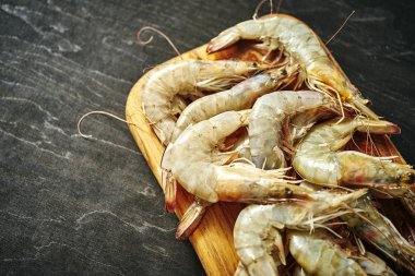 siyah bir tabloda bir ahşap tahta üzerinde taze lezzetli çiğ kaplan karides