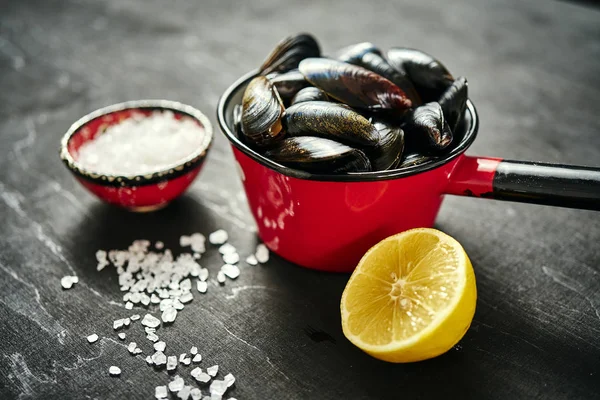 Fresh, delicious raw mussels in a saucepan with salt and lemon — Stock Photo, Image