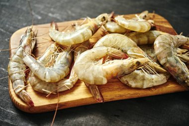 siyah bir tabloda bir ahşap tahta üzerinde taze lezzetli çiğ kaplan karides