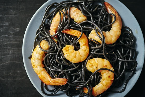 Fresh, delicious black spaghetti with grilled shrimps on a gray plate on a black table — Stock Photo, Image