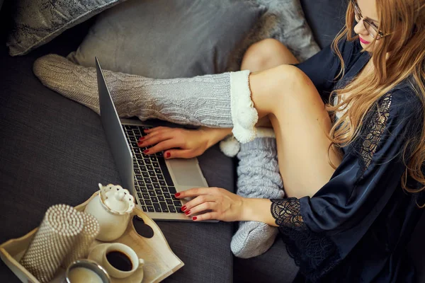 女性の足のビュー グレーのソファーとコーヒーのマグカップ付きのノート パソコン — ストック写真