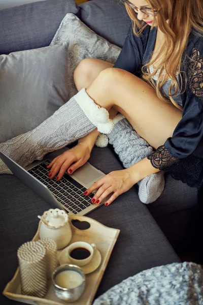 view of a woman's legs on a gray sofa and a laptop with a coffee mug