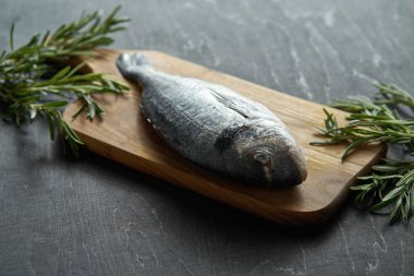 Biberiye, bir taze çiğ dorada balık biber ve tuz bir ahşap tahta ve siyah bir tablo üzerinde