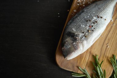 Biberiye, bir taze çiğ dorada balıkla görünümünü op biber ve tuz bir ahşap tahta ve siyah bir tablo üzerinde