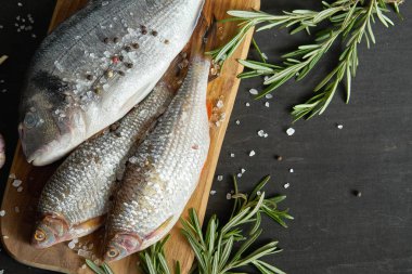 Biberiye siyah bir tabloda bir delikanlı ile ahşap bir tahta üzerinde üç taze çiğ dorada balık üstten görünüm