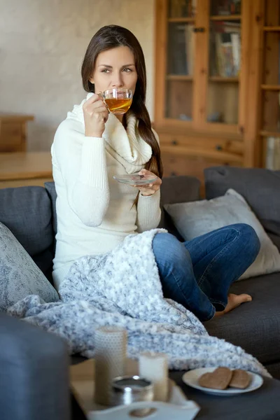 attractive young woman in sweater relaxes on a gray sofa at home and drinks tea with lemon