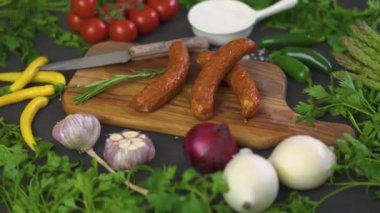 Ahşap oyun tahtası, bıçak siyah bir tabloda farklı sebze ile üç lezzetli sosis