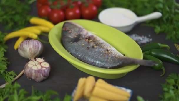 Одна Свежая Сырая Рыба Дорада Зеленом Блюде Набором Овощей Черном — стоковое видео