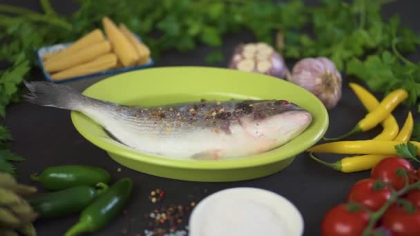 Одна Свежая Сырая Рыба Дорада Зеленом Блюде Набором Овощей Черном — стоковое видео