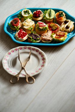 bir grup sağlıklı tapas veya ahşap bir masa üzerinde gıda maşa ile mini sandviç ile eski mavi tepsi