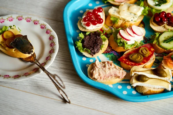 bir grup sağlıklı tapas veya ahşap bir masa üzerinde gıda maşa ile mini sandviç ile eski mavi tepsi