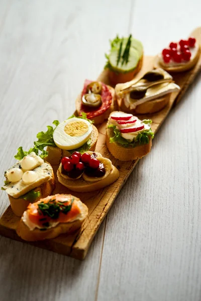 Деревянная доска с красочными здоровыми мини-бутербродами или тапас на деревянном столе — стоковое фото