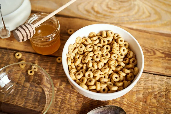 Café da manhã saudável tigela cheia de flocos de mel com mel dipper e leite em uma mesa de madeira — Fotografia de Stock