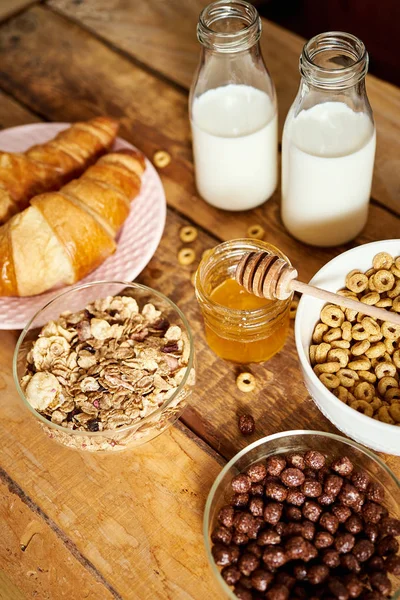 Colazione sana con diversi tipi di cereali per la colazione con cucchiaio, croissant al miele e latte — Foto Stock