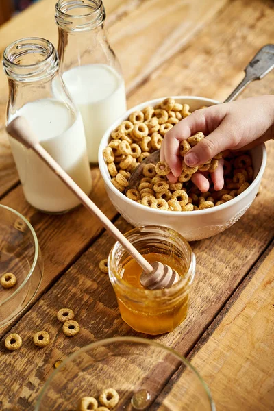 Crianças mão segurando tigela com café da manhã saudável com flocos mel leite e mel dipper na mesa — Fotografia de Stock